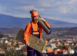 man in hard hat carrying roofing supplies