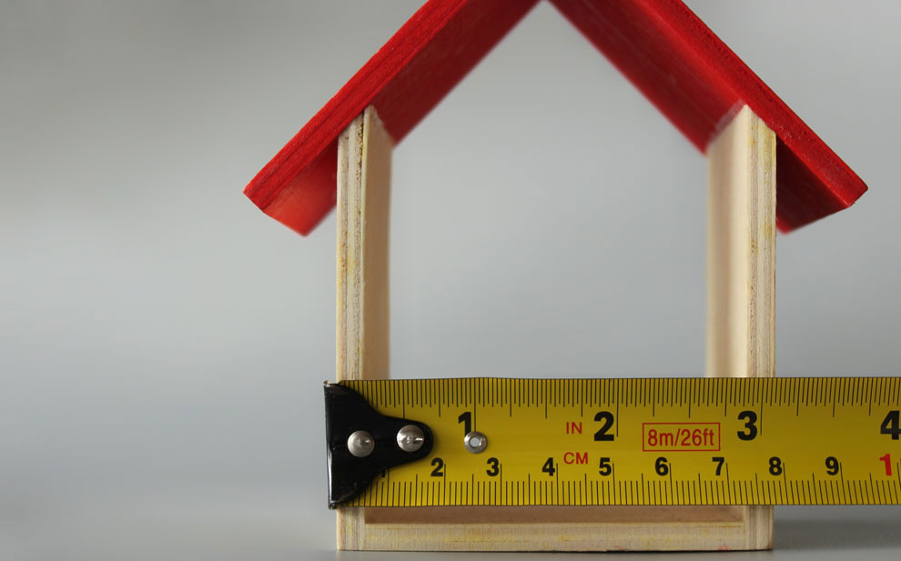 Miniature house with red roof and measuring tape for Garvey Roofing Free Estimates