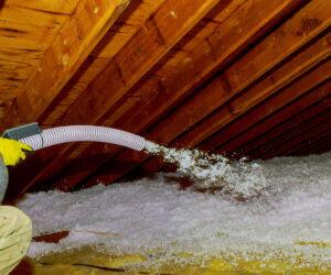 Man holding a blow-in fiberglass insulation on the attic floor.